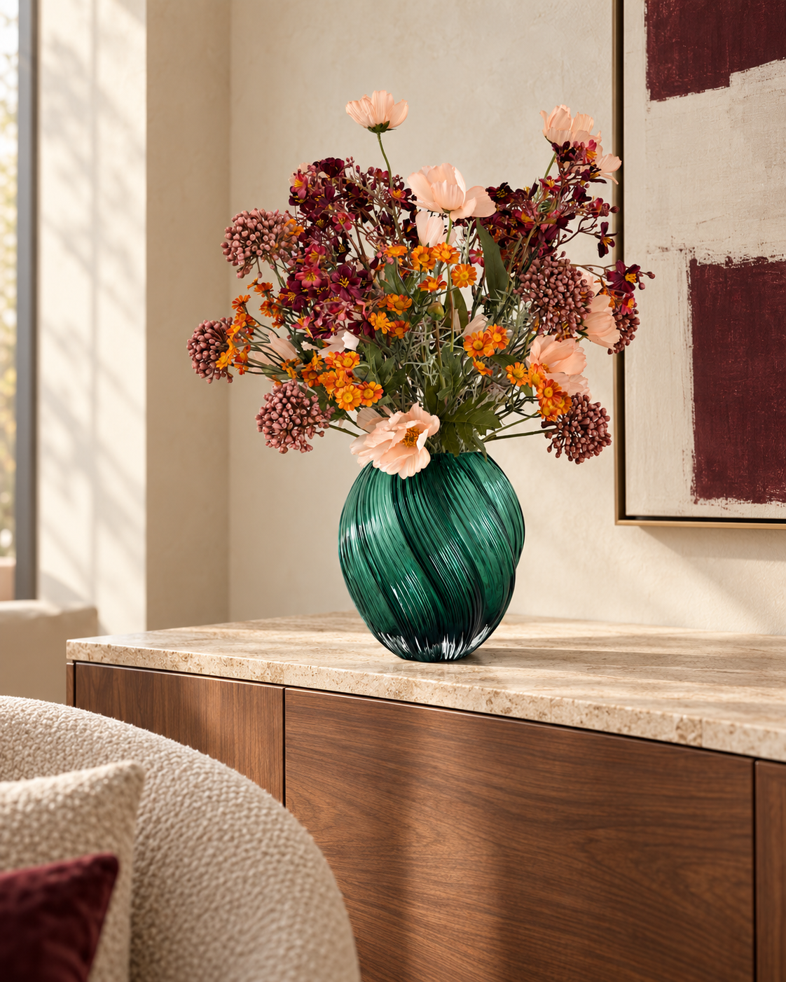 Amber Meadow, zijden boeket in abrikoos, oranje en bordeaux in een diepgroene glazen vaas op een dressoir in een interieur .