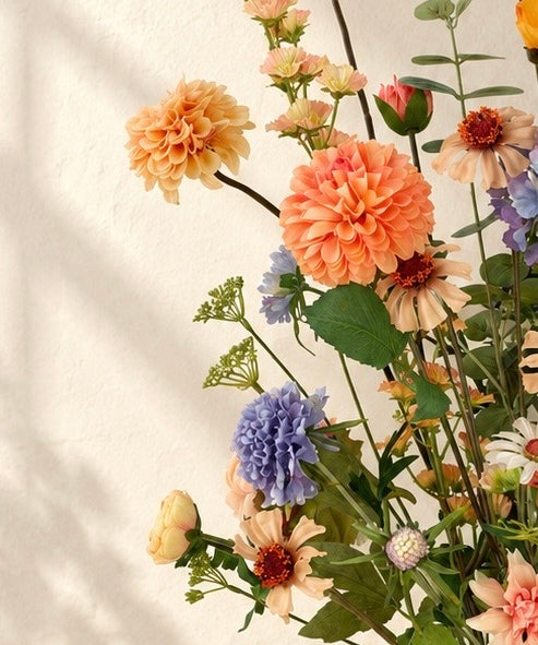 Detail van Apricot Garden zijden boeket met abrikooskleurige, oranje, lila en blauwe bloemen in een matte zandkleurige vaas.
