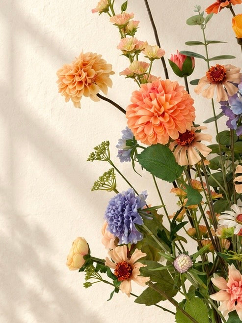 Detail van Apricot Garden zijden boeket met abrikooskleurige, oranje, lila en blauwe bloemen in een matte zandkleurige vaas.