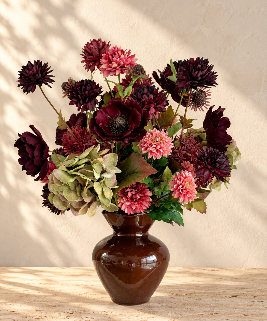 Velvet Muse zijden boeket met bordeaux en roze bloemen en groene hortensia’s in een glanzende bruine vaas op travertin.