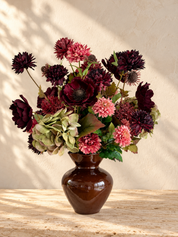 Velvet Muse zijden boeket met bordeaux en roze bloemen en groene hortensia’s in een glanzende bruine vaas op travertin.
