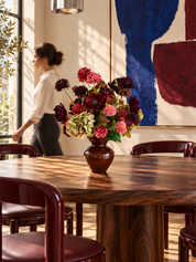 Velvet Muse zijden boeket in een bruine vaas op een notenhouten eettafel, met een bordeaux muur en zacht ochtendlicht.