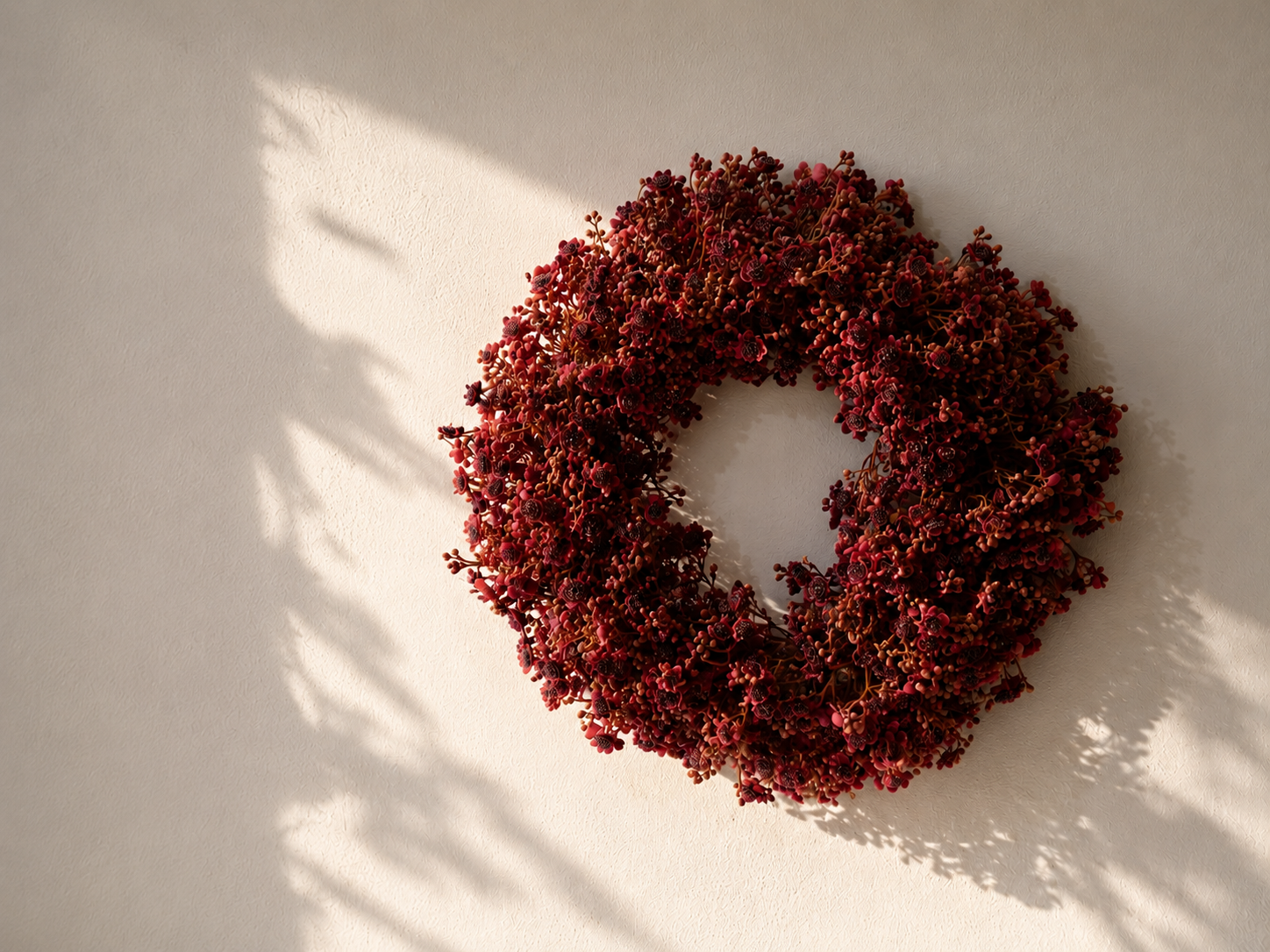Bordeaux bloemenkrans 30 cm aan beige muur met natuurlijk ochtendlicht