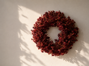 Bordeaux bloemenkrans 30 cm aan beige muur met natuurlijk ochtendlicht
