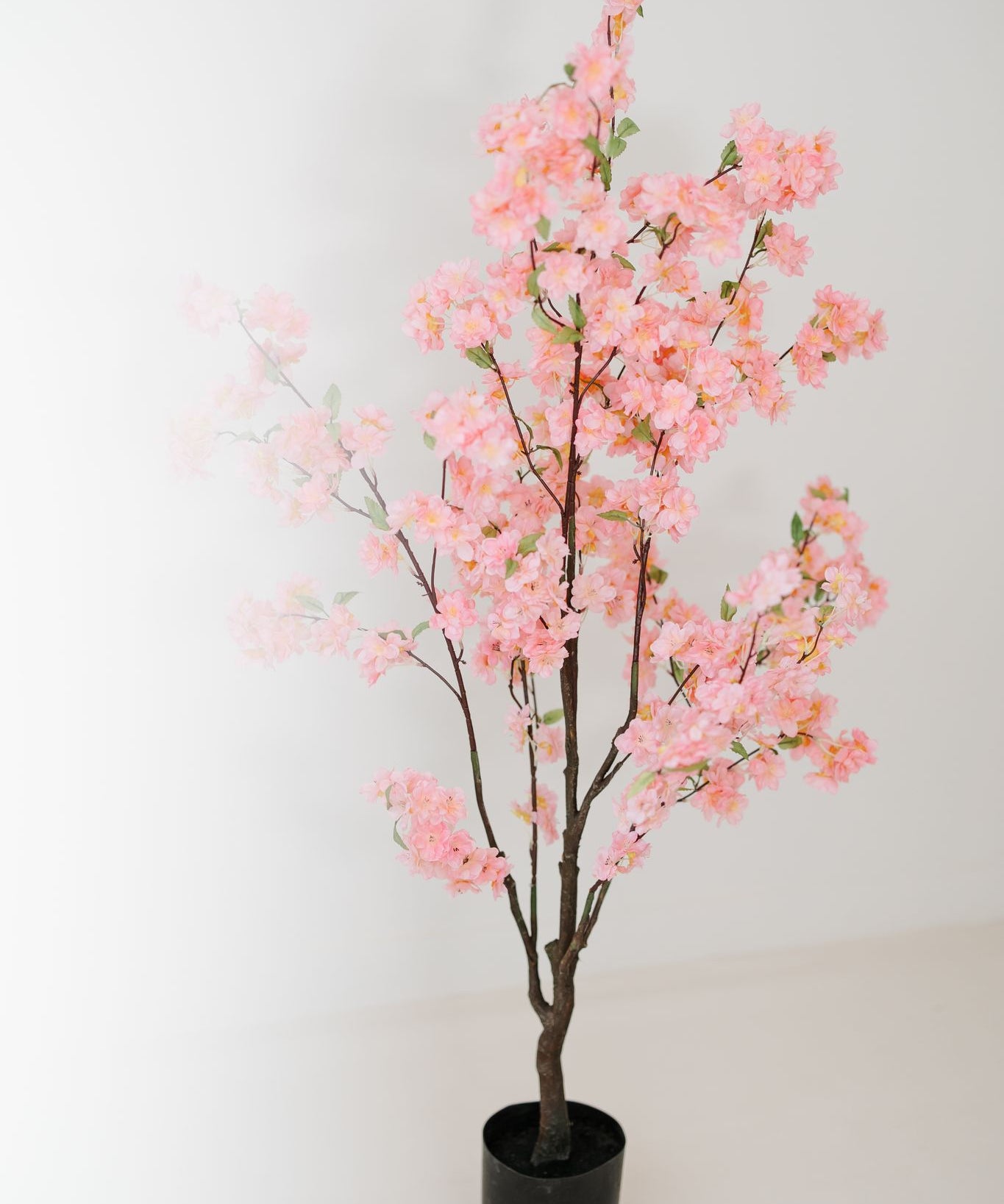 Roze kunst bloesemboom van 135 cm in zwarte pot tegen lichte achtergrond