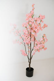 Roze kunst bloesemboom van 135 cm in zwarte pot tegen lichte achtergrond