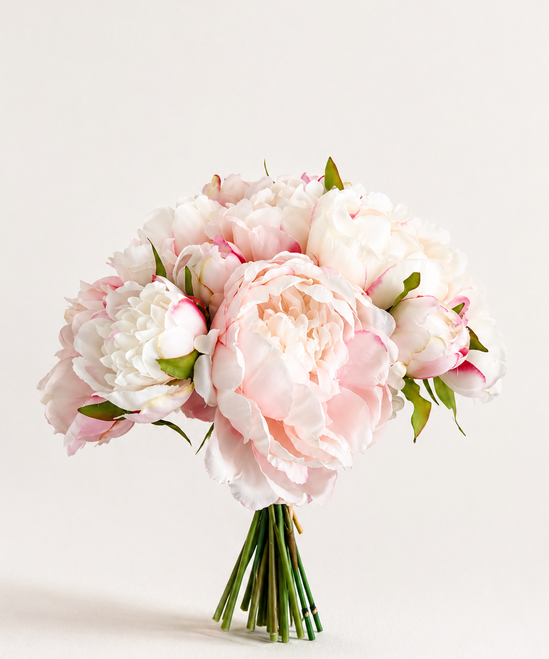 Zijden pioenrozen boeket in zacht roze en wit met volle bloemen op lichte achtergrond
